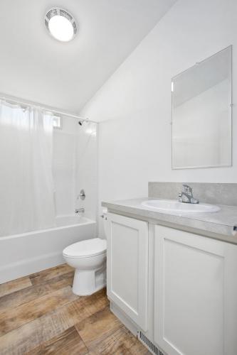 Bathroom with white walls, toilet, sink, shower.